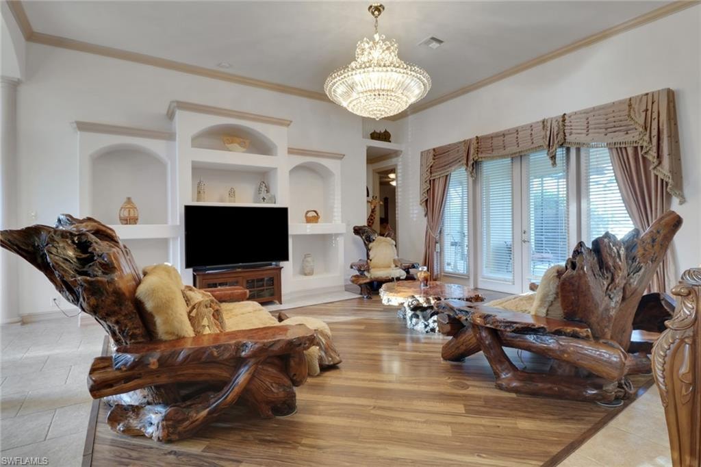 Living area with built in features, ornamental molding, light tile patterned flooring, and a chandelier