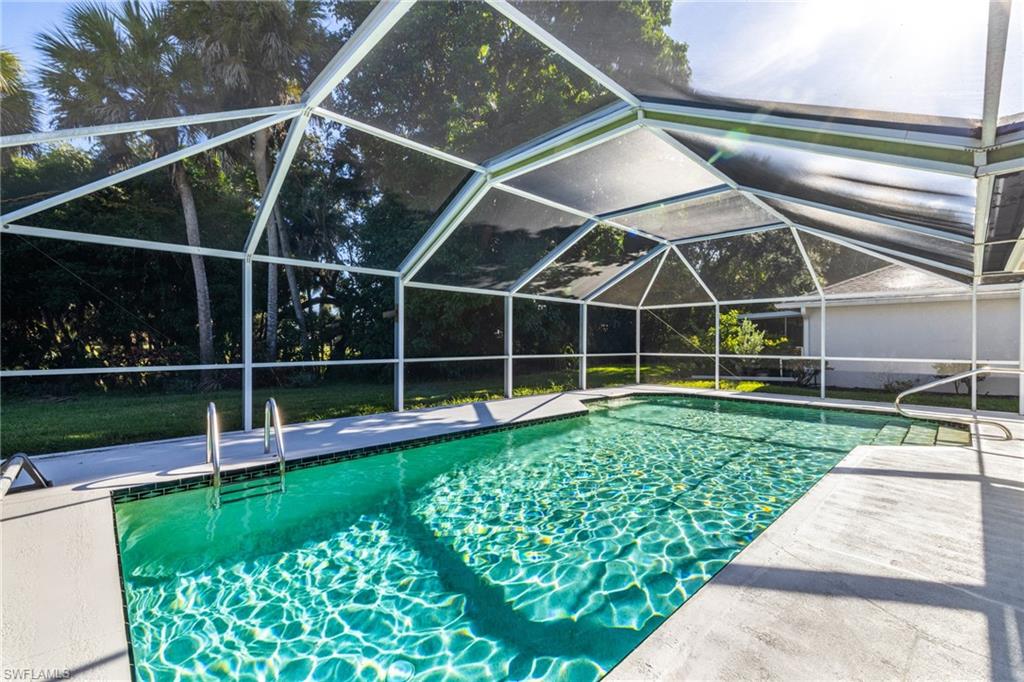 Screened-in swimming pool featuring a concrete deck, built-in steps, and a handrail