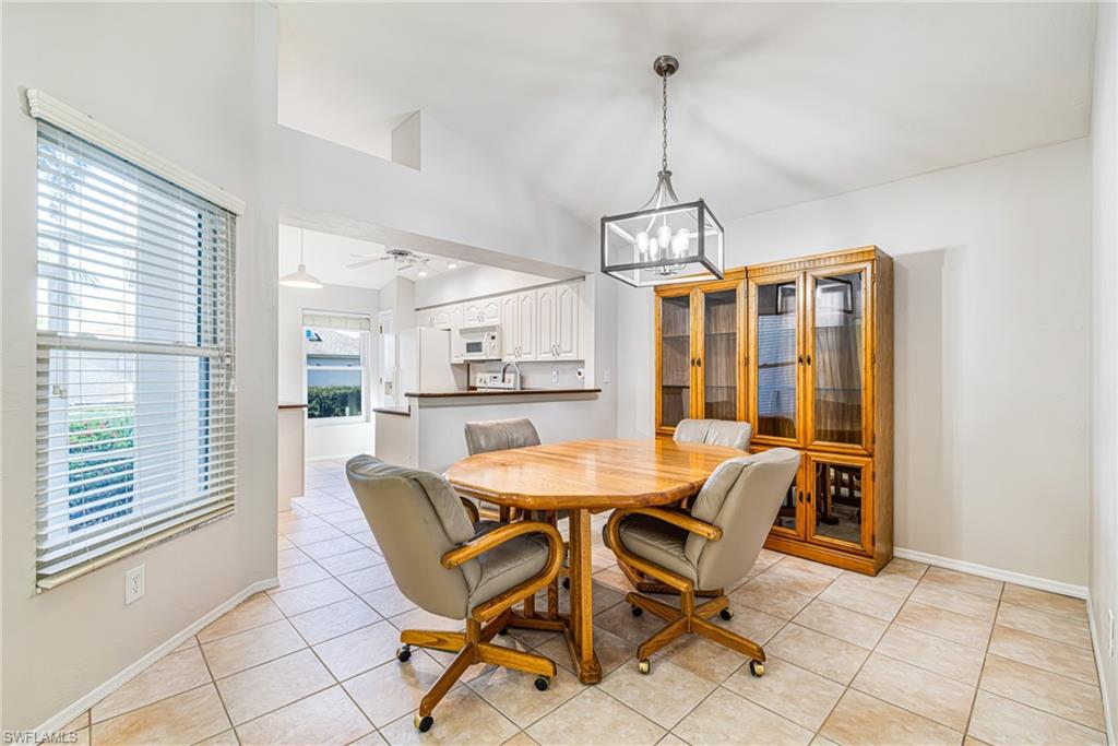 Vaulted ceiling with a contemporary chandelier, tile flooring, and a window with blinds