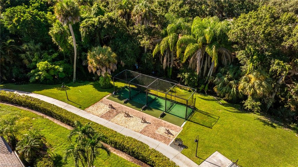 Turf hitting bays with protective netting, paver-style hardscaping, manicured lawn, and mature tropical foliage