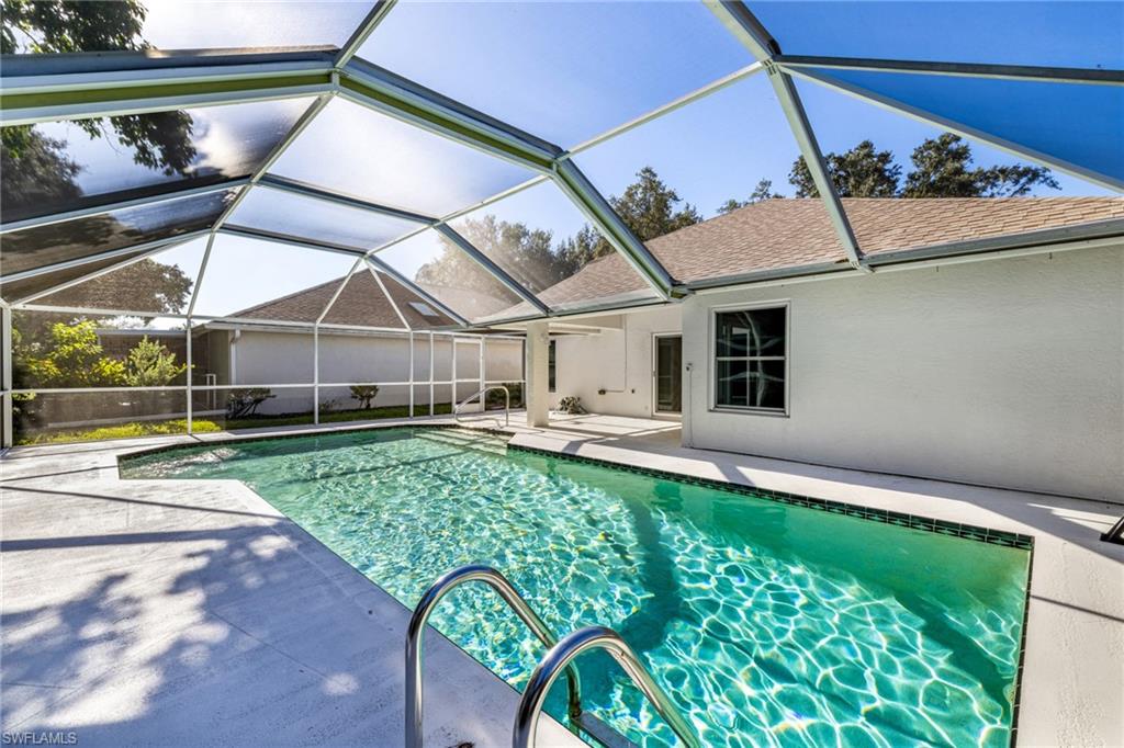 Screened-in swimming pool with a surrounding patio, featuring a white stucco exterior and a shingled roof