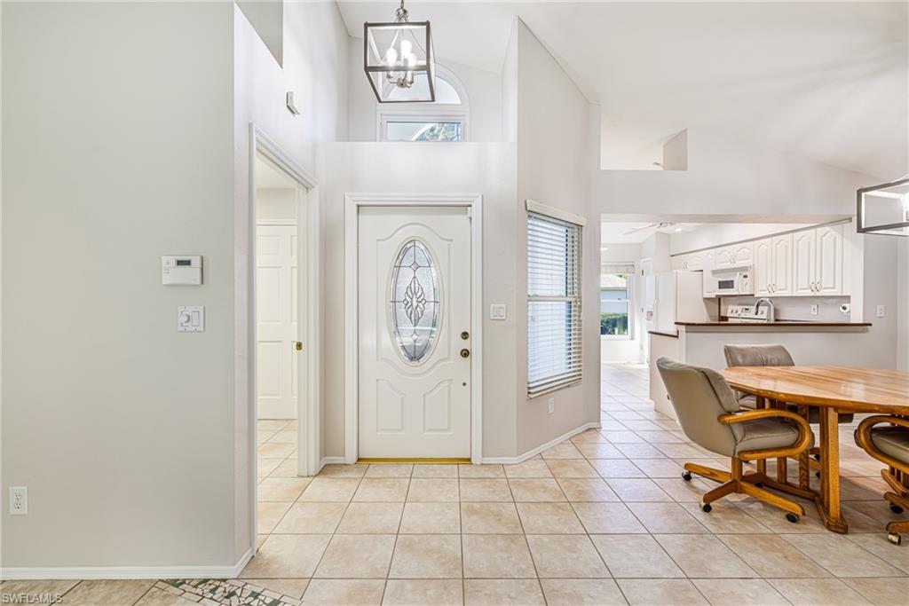 Tiled entryway with a decorative glass front door, vaulted ceilings, and a contemporary pendant light fixture