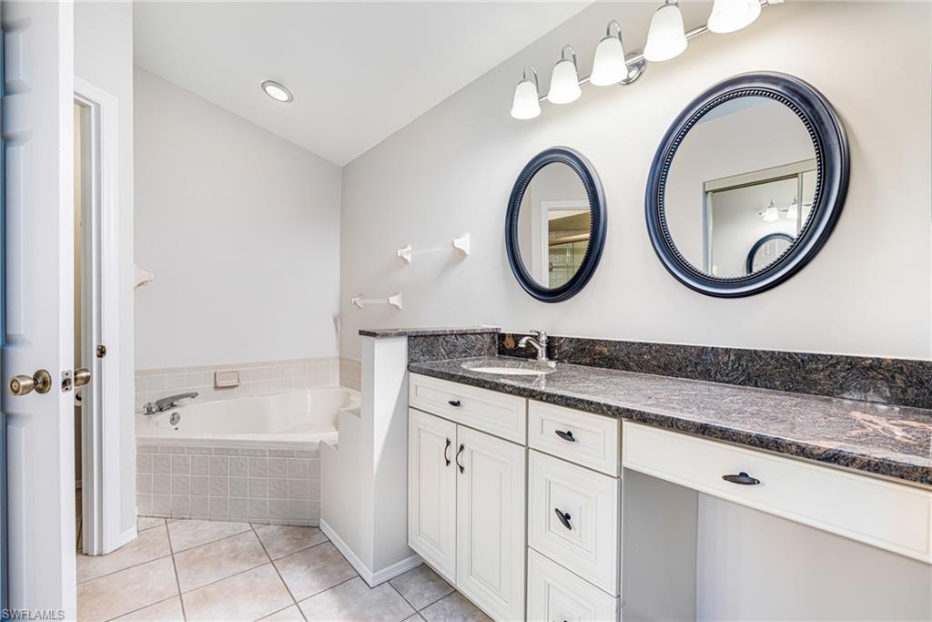 Dual vanity with dark countertops, built-in makeup area, two framed circular mirrors, and white cabinetry