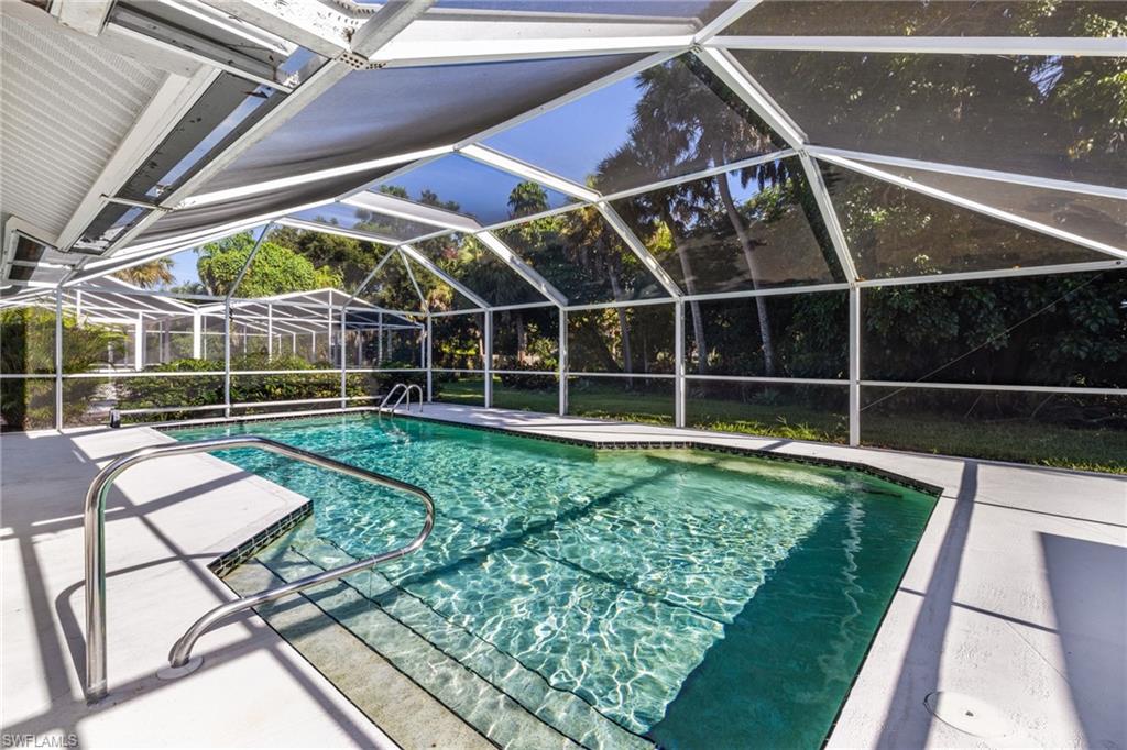 Screened pool enclosure featuring a rectangular swimming pool with integrated steps, a handrail, and surrounding concrete decking
