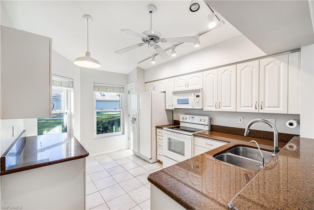 Bright, open kitchen featuring white cabinetry with brushed nickel hardware, wood-finish countertops, stainless steel sink with curved faucet, white tile flooring, and abundant natural light from multiple windows overlooking the oceanfront