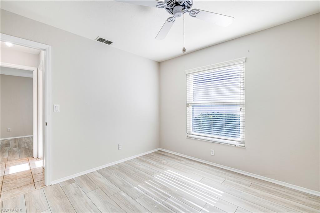 Light-toned wood-finish flooring, white walls, ceiling fan with light fixture, window with blinds