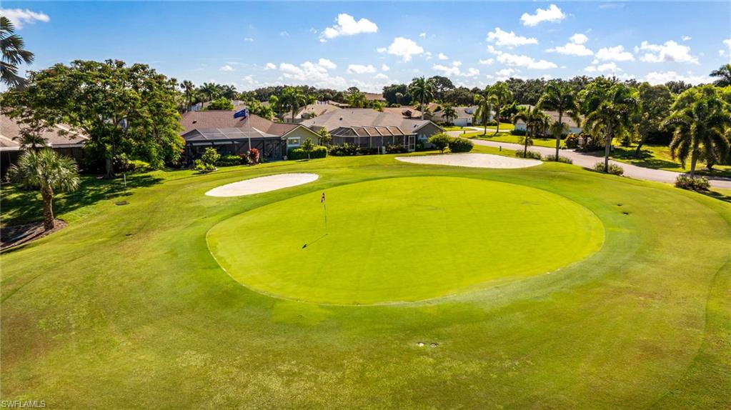 Manicured golf course green with sand traps, surrounded by mature palm trees and residential properties