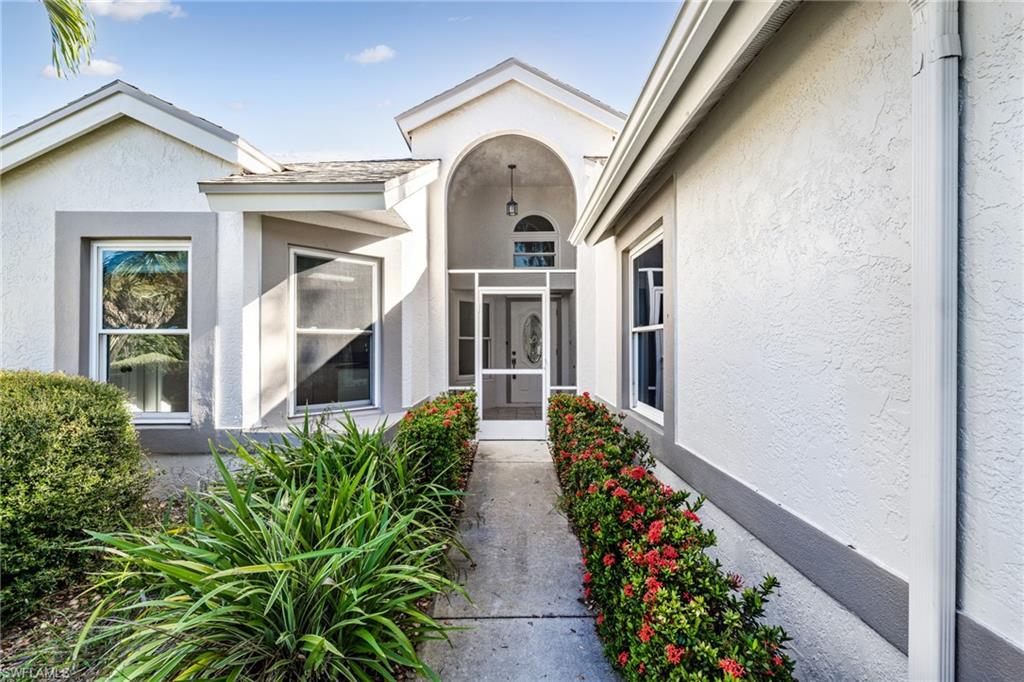 Property exterior featuring a stucco finish, arched entry, screened front door, and established landscaping