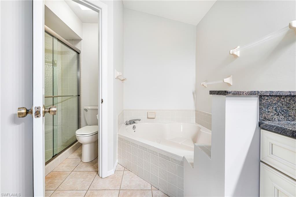 Built-in corner bathtub, tiled tub surround, stone countertop, white cabinetry, and a shower with glass enclosure