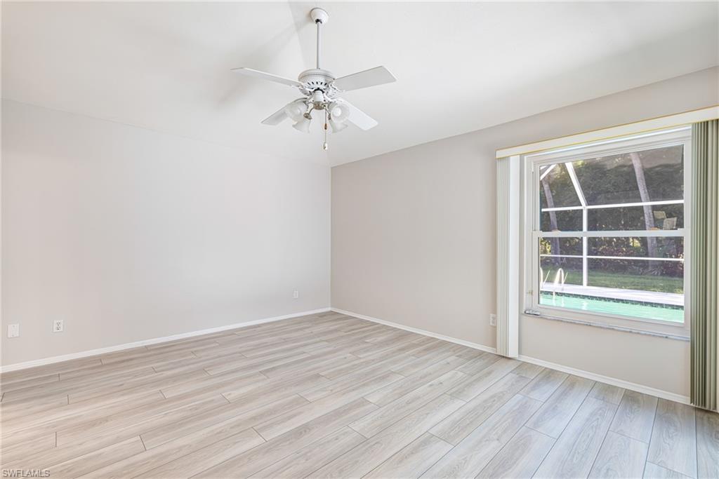 Spacious room featuring wood-finish flooring, a ceiling fan with light fixture, and a large window overlooking an outdoor area with a pool