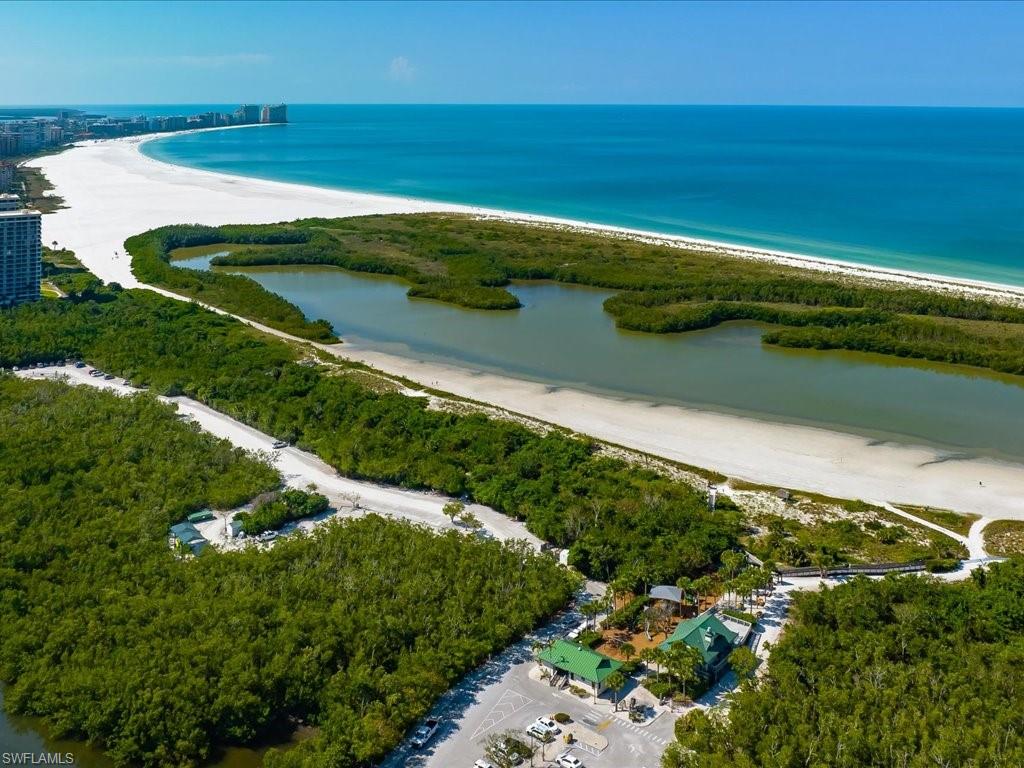 Expansive white sand beachfront, clear blue waters, lush green vegetation, and nearby urban development