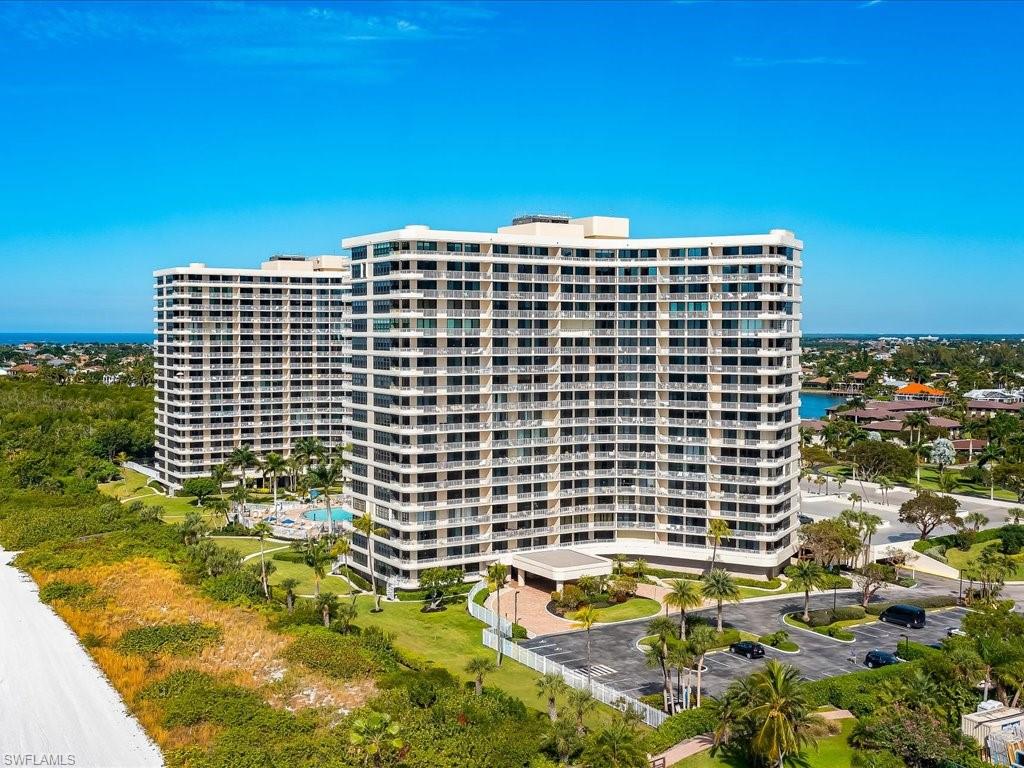 Twin high-rise buildings featuring multiple balconies, a ground-level swimming pool, and extensive landscaping with palm trees