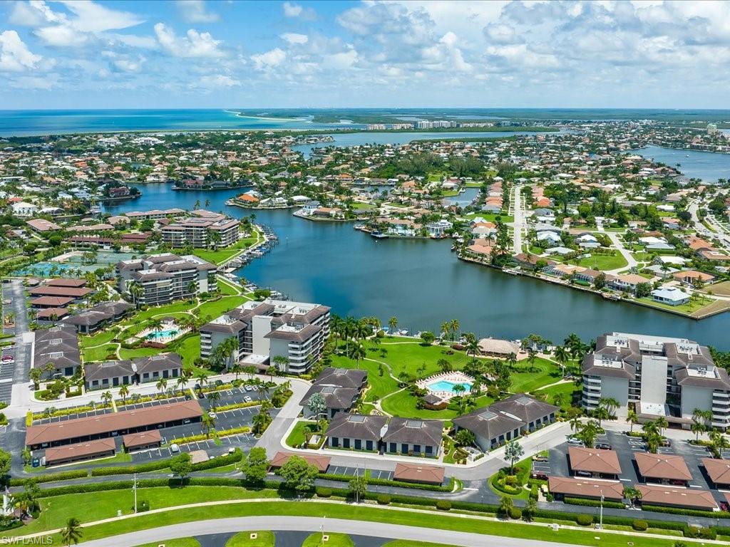 Waterfront community with multiple buildings featuring a swimming pool, tennis courts, and mature landscaping