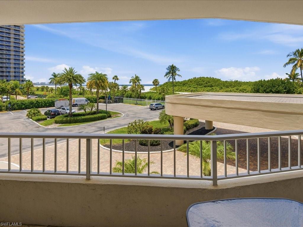 Balcony with metal railing overlooking a paved circular drive, palm trees, and distant water