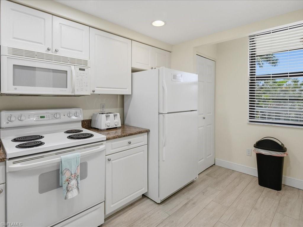 White cabinetry, built-in microwave, white electric range, wood-finish flooring, and a window with horizontal blinds