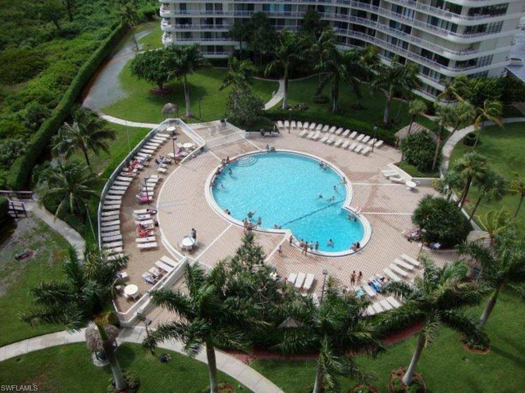 Expansive freeform swimming pool with surrounding paver decking, curved terraced seating, multiple lounge areas, and lush tropical landscaping