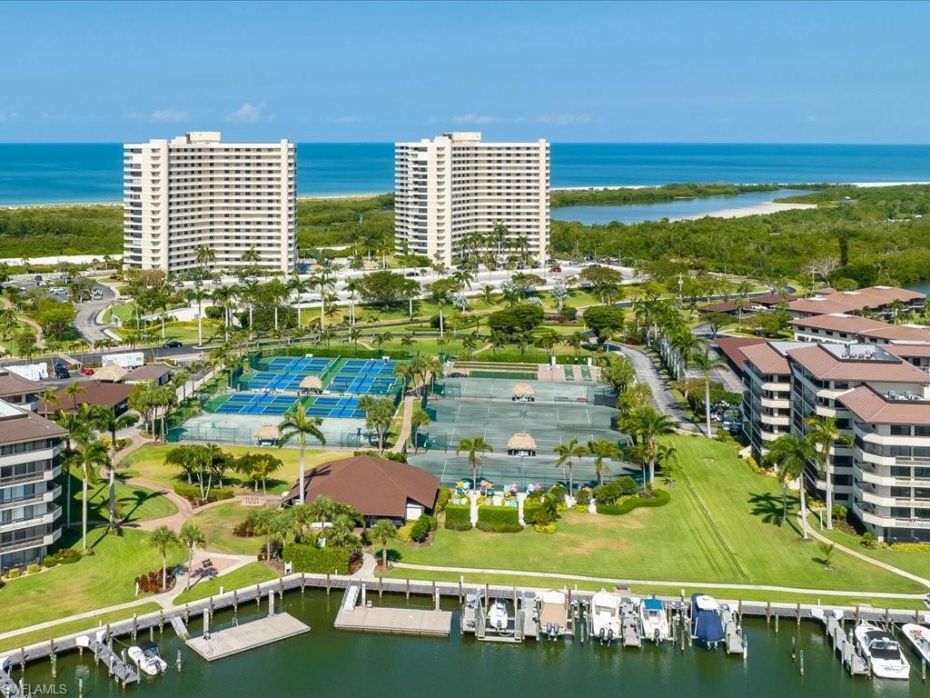 Waterfront marina with multiple boat slips, extensive tennis court facilities, mature landscaping, and multi-story residential buildings