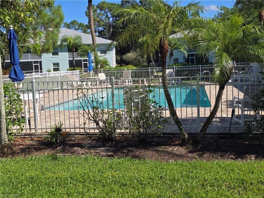 Community swimming pool with surrounding paver deck, white metal fencing, and mature palm trees