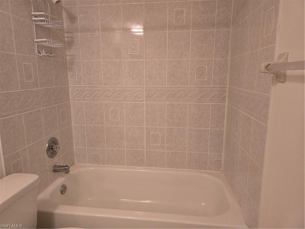White porcelain bathtub with chrome fixtures and light-colored tiled surround featuring decorative border tiles
