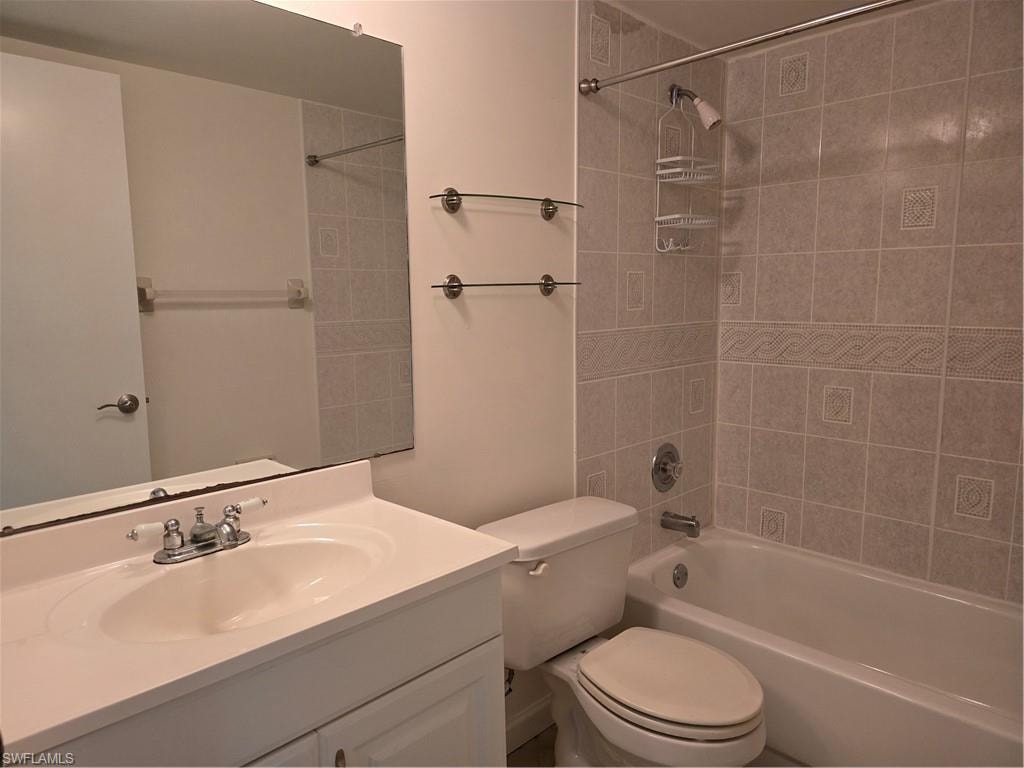 Bathroom featuring a vanity with an integrated sink, polished chrome faucet, full-width mirror, tile shower surround, and a built-in bathtub