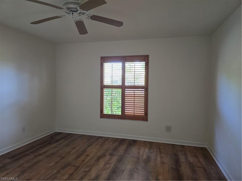 Wood-finish flooring with white baseboards, window with wooden plantation shutters, and ceiling fan with integrated lighting