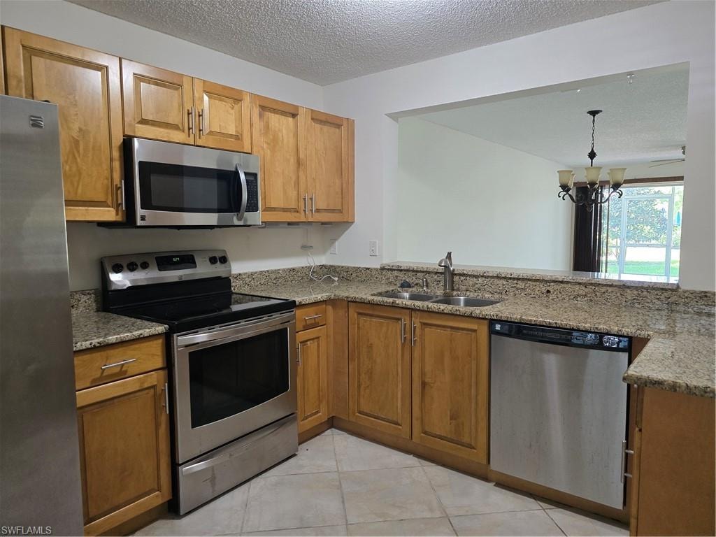 Kitchen featuring wood cabinetry, light-toned countertops, stainless steel appliances, and a pass-through opening
