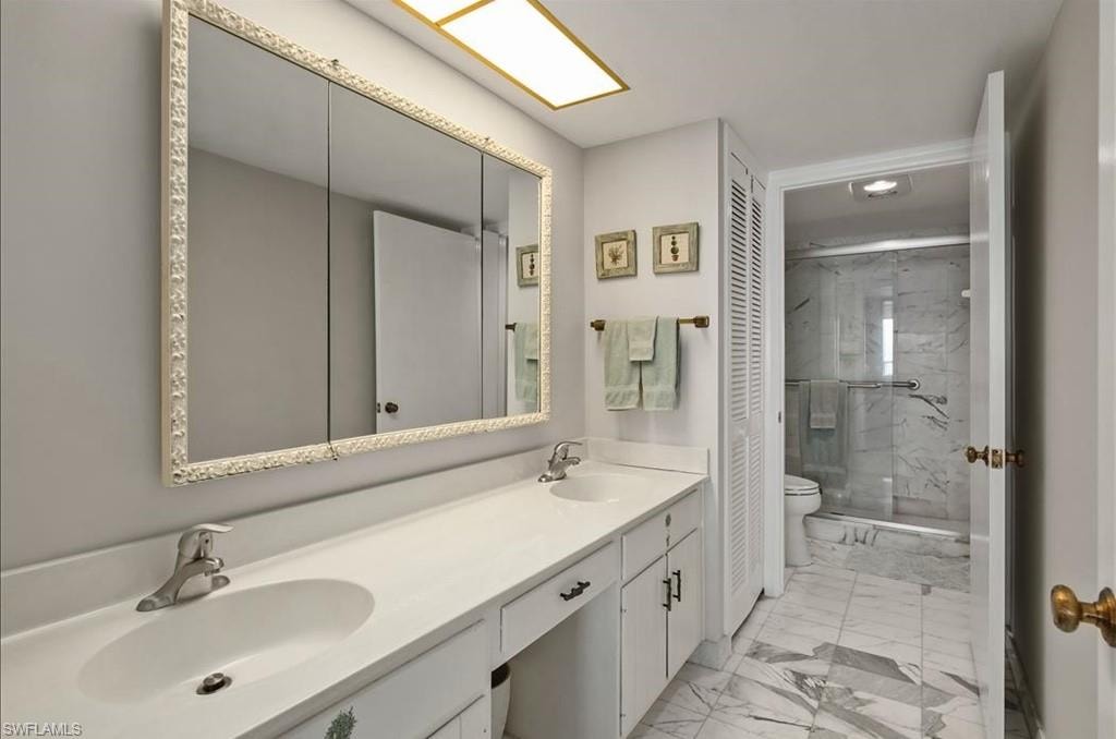 Full bath featuring marble look tile flooring, a marble finish shower, and double vanity