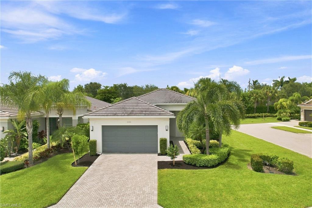 Tile roof residence featuring an attached garage, paver driveway, manicured lawn, and mature landscaping