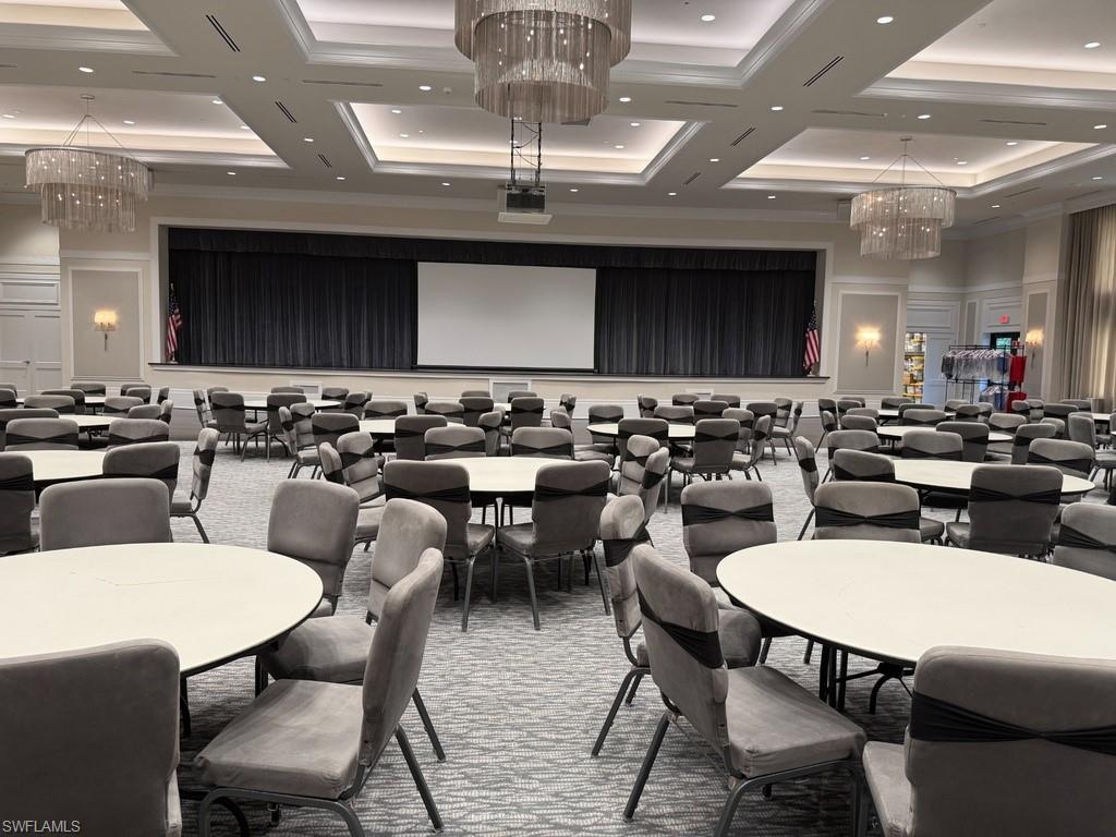 Spacious event hall featuring a stage with dark drapery, recessed lighting, and elegant tiered chandeliers