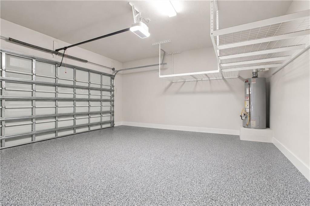 Garage featuring epoxy flooring, overhead storage racks, a utility water heater, and an automatic garage door opener
