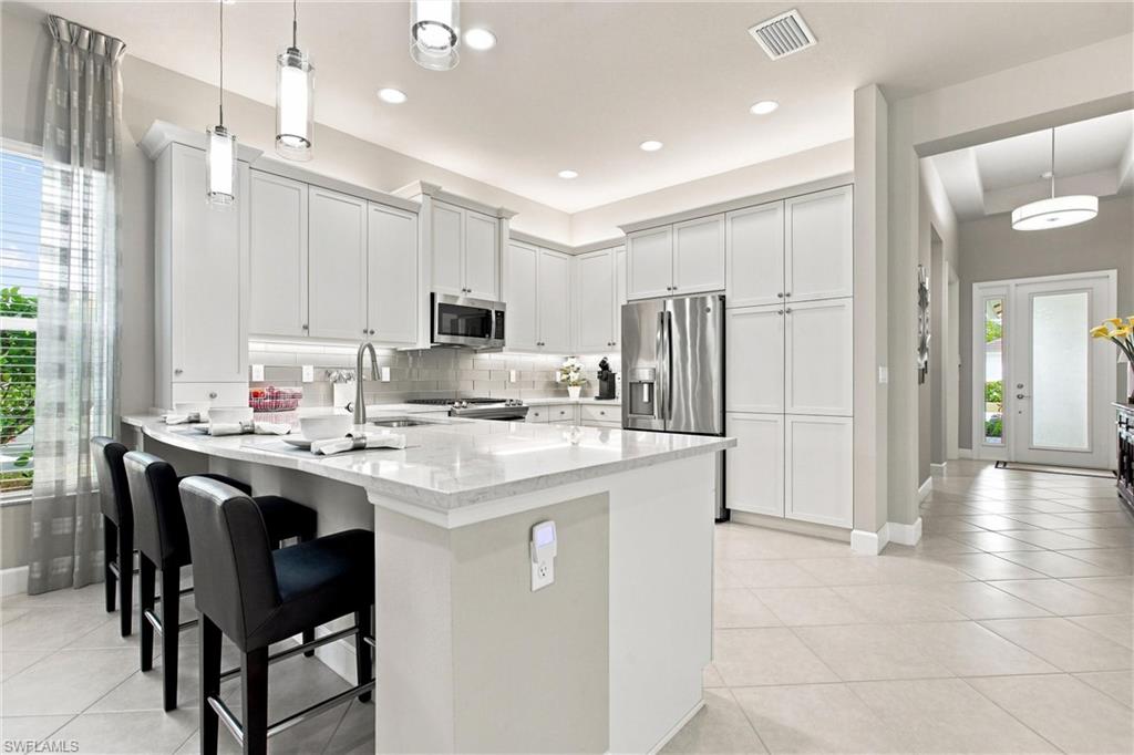 Kitchen featuring white shaker cabinetry, stainless steel appliances, a white stone countertop island with seating, pendant lighting, and tiled flooring