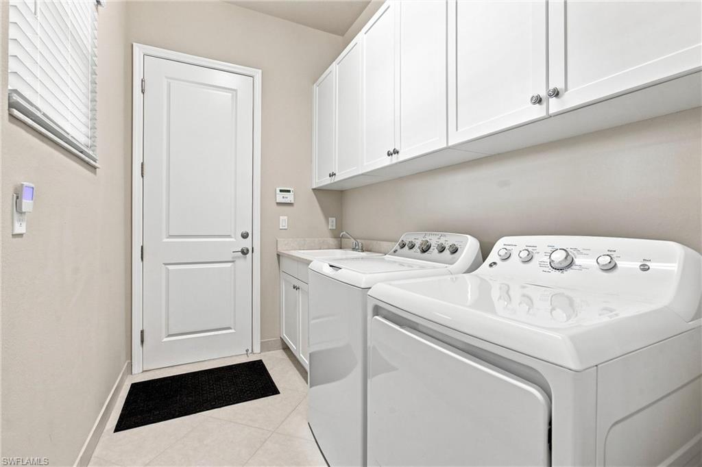 Laundry room featuring white cabinetry, a sink with a faucet, and light-toned tile flooring