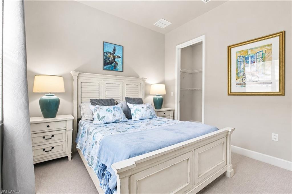 Bright and serene primary bedroom featuring a white wooden bed frame with paneled headboard, dual nightstands with ceramic table lamps, soft carpet flooring, recessed ceiling lighting, and neutral wall finishes