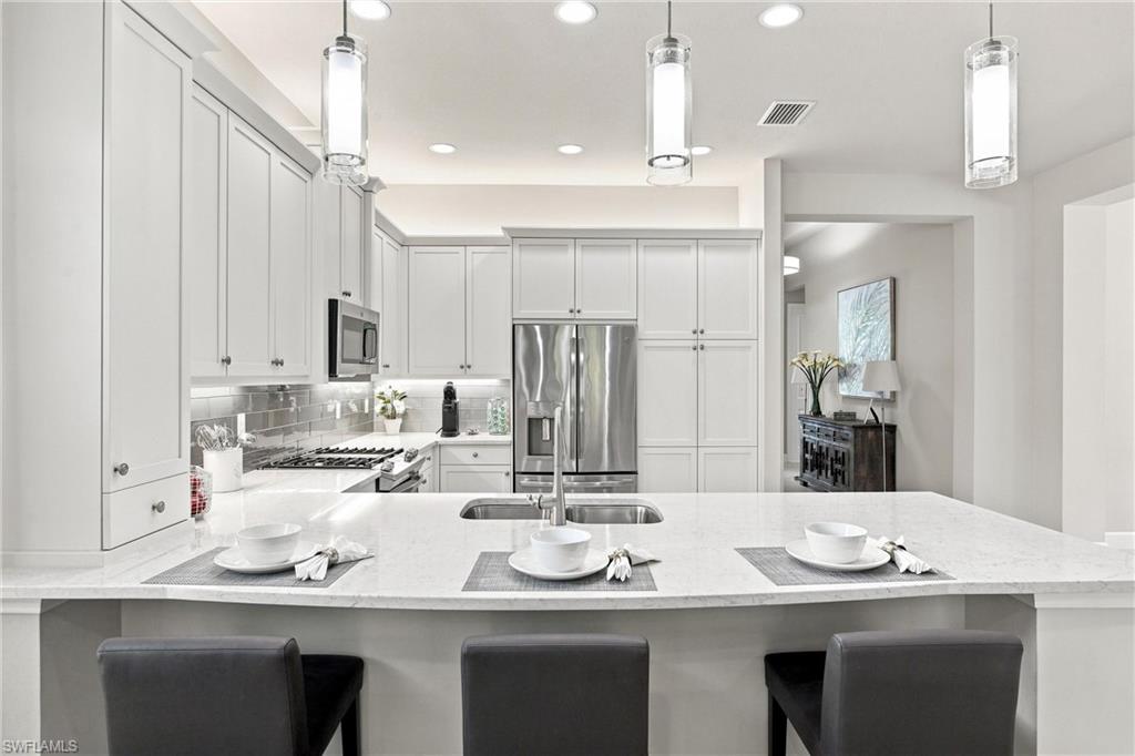 Kitchen with white shaker-style cabinetry, stainless steel appliances, a tile backsplash, and a large island with an undermount sink