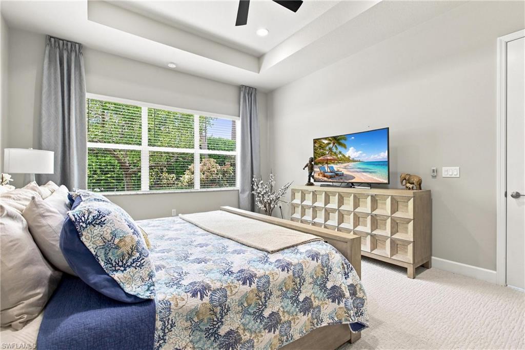Tray ceiling with recessed lighting, ceiling fan, large window with blinds, and light-colored carpet