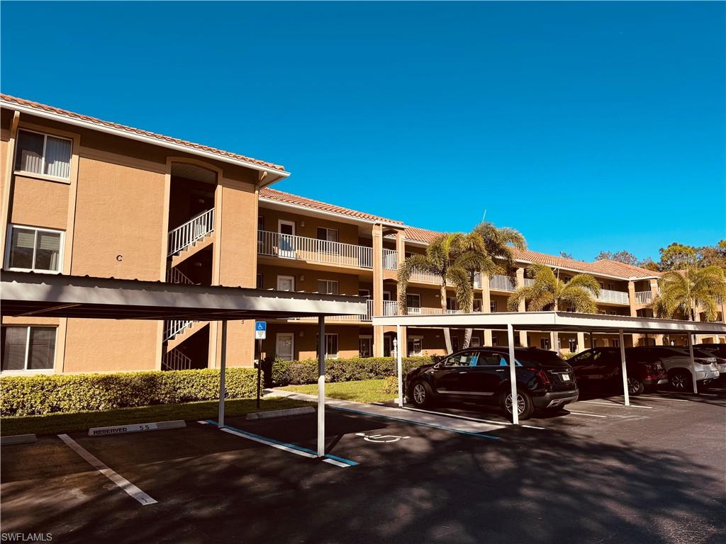 Multi-story building with a stucco exterior, tile roof, covered parking, and mature palm trees