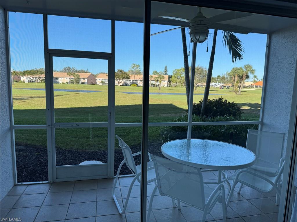 Screened patio with tiled flooring and a ceiling fan, overlooking a landscaped green space