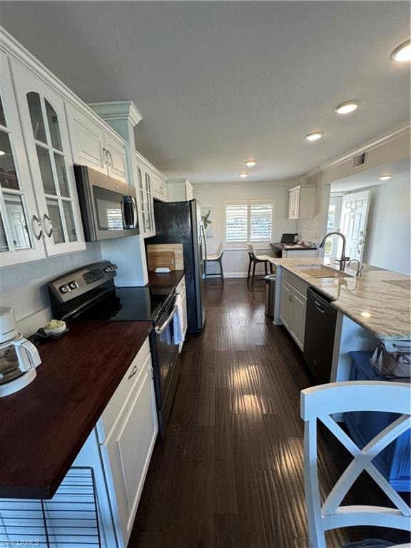Kitchen featuring wood-finish flooring, white cabinetry, dark wood-finish countertops, stainless steel appliances, and an island with a stone countertop and built-in sink