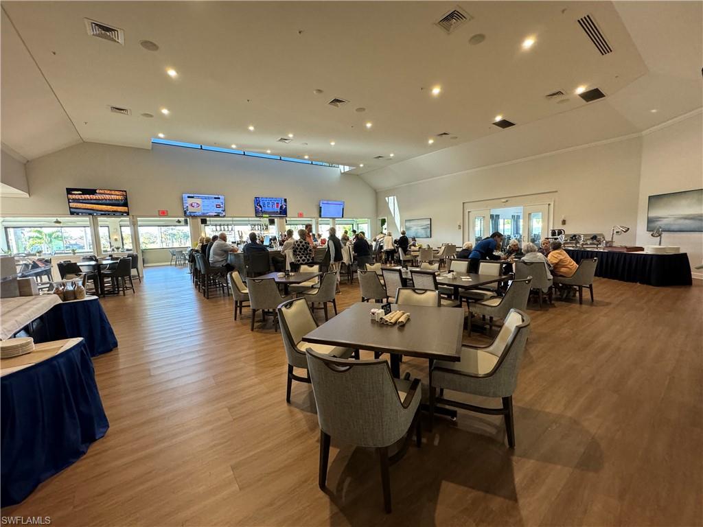 Spacious common area featuring vaulted ceilings, wood-finish flooring, a built-in bar, recessed lighting, and large windows