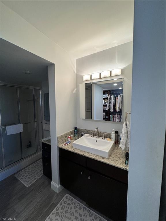 Wood-finish flooring, dark wood vanity with ample storage, light speckled countertop, vessel sink with chrome fixtures, and a glass-enclosed shower