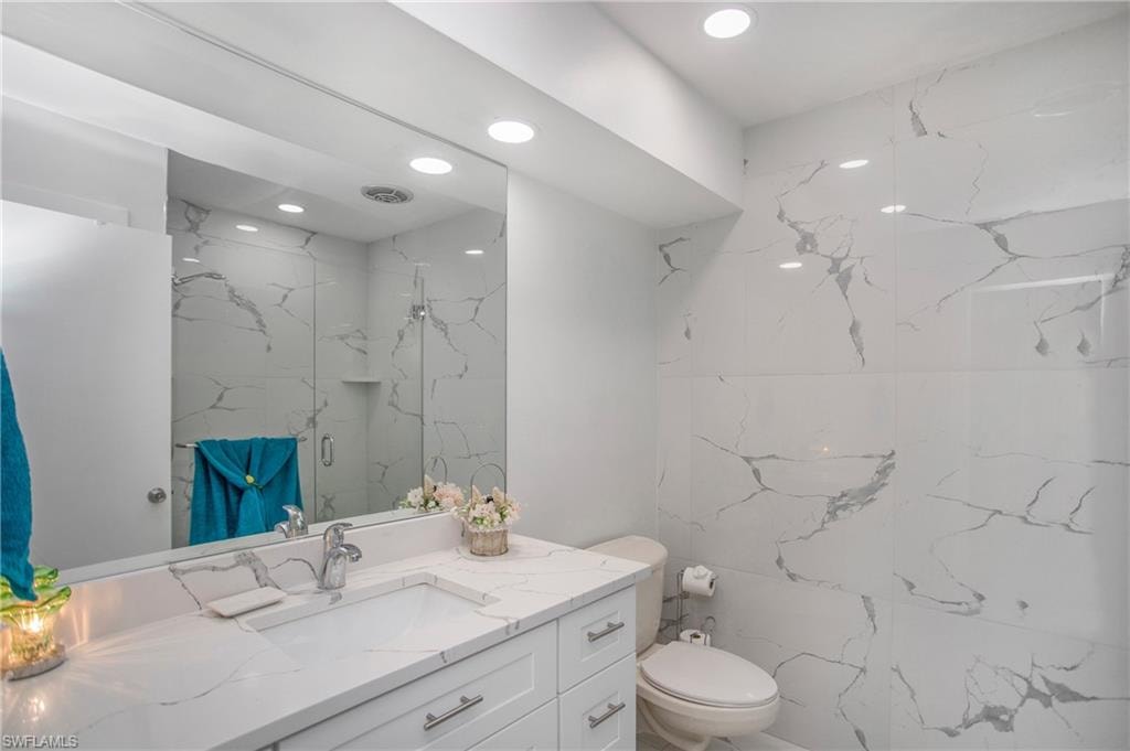Recessed lighting illuminating a vanity with a white countertop and an integrated sink, complemented by a full-width mirror and floor-to-ceiling tile in a marbled pattern