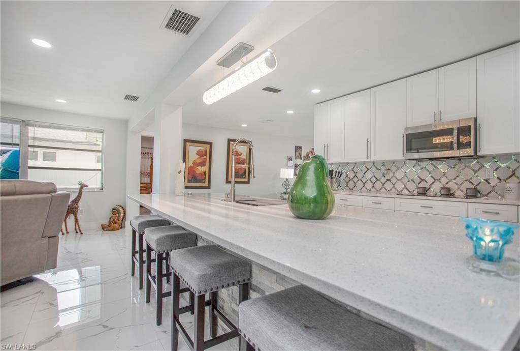 White cabinetry with stainless steel appliances, mosaic tile backsplash, and a large central island with seating