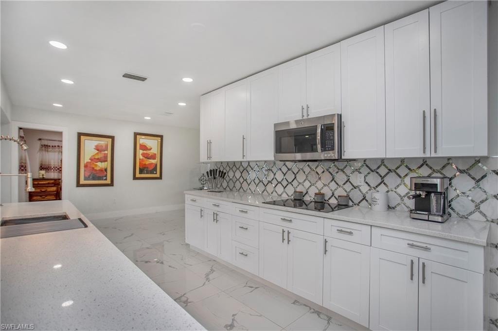 White shaker-style cabinetry with stainless steel hardware, integrated stainless steel microwave, cooktop, and a patterned tile backsplash