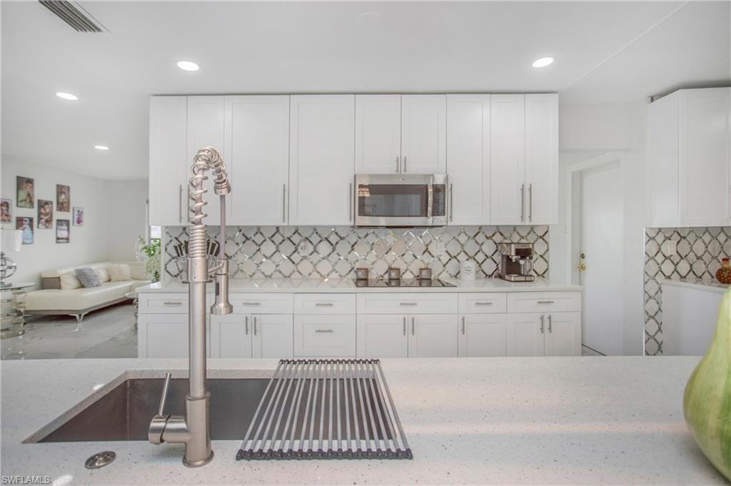 Modern kitchen featuring white cabinetry, a patterned tile backsplash, stainless steel appliances, a large sink with a coil spring faucet, and recessed lighting