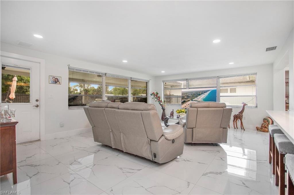 White tile flooring with grey veining, recessed lighting, white walls, multiple windows, and a white interior door with a glass panel