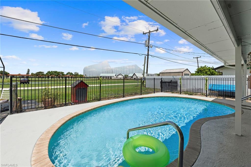 In-ground swimming pool with a concrete surround and metal coping, complemented by a black metal fence and an expansive grassy area