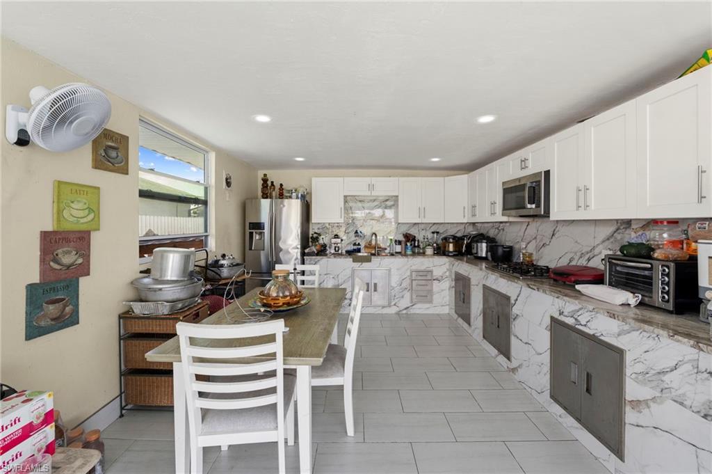 White shaker cabinetry, stainless steel appliances, patterned marble-look countertops, tiled flooring, and recessed lighting