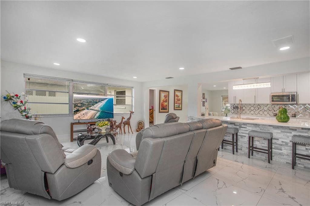 White large-format tile flooring, recessed ceiling lighting, kitchen island with stone veneer base, stainless steel microwave, and white cabinetry