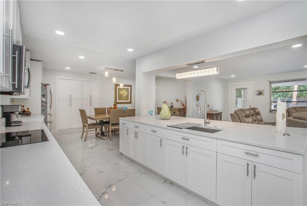 Kitchen featuring white cabinetry, light-toned countertops, a built-in cooktop, and a stainless steel sink with a gooseneck faucet