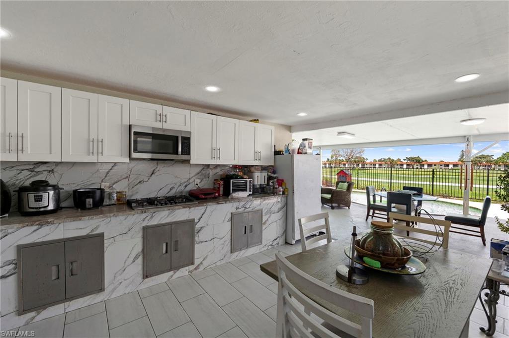 Outdoor kitchen featuring a gas range, stainless steel microwave, white shaker-style cabinetry, and stone countertops